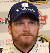 A man in his early 40s sporting a full face beard and wearing a baseball cap with a sponsors logo.