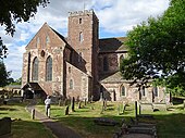 Photographie couleur d'une église en pierre rosée au milieu d'un cimetière.