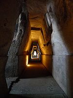 A dark stone corridor with light at the distant end