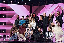 Foto von 17 Personen, die für ein Gruppenfoto auf einer Bühne stehen