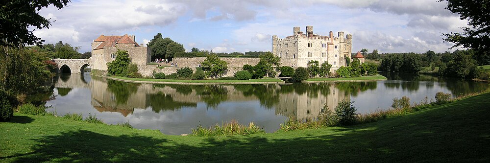 A castle on two islands surrounded by a lake. A stone curtain wall runs along the edge of the first island and access is provided by a stone bridge and gatehouse. The second island has a square stone keep.