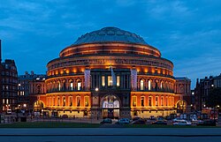 Bagian luar gedung bulat dengan spanduk besar mempromosikan prom BBC pada hari yang cerah