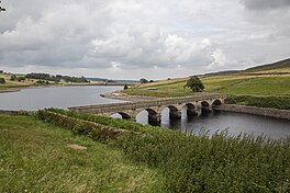 Image of a reservoir, with a six-arch stone bridge in the foreground spanning the water