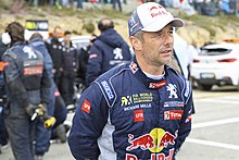 Photo de Sébastien Loeb vu de face en combinaison automobile.