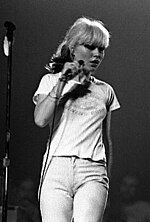 Singer Debbie Harry is shown onstage at a concert. She is wearing jeans and a T-shirt.