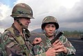 Instrutor (à esquerda) durante o exercício Orient Shield '85, em 17 de novembro de 1985, com a camuflagem Woodland em seu capacete e uniforme, a qual foi projetada principalmente para operações da OTAN.