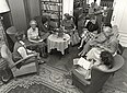 Schwarz-Weiß-Fotografie eines Bibliotheksraumes, in dem mehrere Frauen im Rund sitzen und sich unterhalten; im Nebenzimmer sitzt eine Frau am Schreibtisch