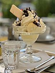 A glass bowl of vanilla ice cream with whipped cream, chocolate syrup, and a wafer