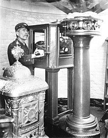 Keeper E.J. Moore circa 1918 standing next to a Fresnel mechanical flash mechanism and holding its crank.