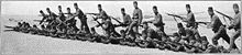 photographie noir et blanc : des soldats armés de fusils à la manœuvre : une moitié debout, une moitié au sol