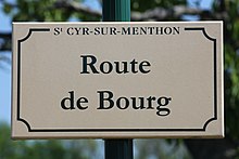 Plaque de rue de couleur blanche où est inscrit Route de Bourg écrit en vert.
