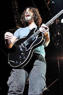 Photographie d'un homme debout sur scène jouant de la guitare.