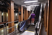 An escalator leading from the Canarsie Line platform to the Lexington Avenue Line platform's mezzanine. There are brown columns on either side.