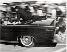 Agent Hill se tiskne ke Kennedyho limuzíně (22. listopad 1963, Dallas, Texas)