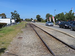 A railroad line adjacent to a road. A switch can be seen in the background.