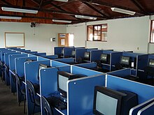 A computer lab, showing a number of desks containing CRT monitors, and the associated seating, with blue dividers in between individual workstations