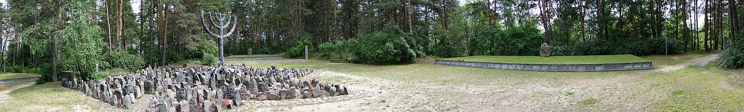 Panorama foto de la loko: dekstre estas la amastombo, maldekstre estas monumento en formo de Menoro kaj ĉirkaŭ ĝi estas ŝtonoj aranĝitaj en la formo de la Davida stelo kaj sur ili estas gravuritaj la nomoj de iuj el la murditoj.