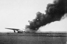 Photo noir et blanc d'une carcasse d'avion entourée d'une épaisse fumée noire.