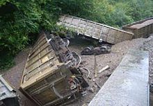 Three railway stone wagons, resting at a variety of angles, two overturned, with no tracks in view