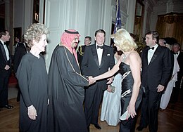 Ivana Trump n' Mackdaddy Fahd shake hands, wit Ronald Reagan standin next ta dem smilin fo' realz. All is up in black formal attire.