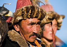 Photo montrant le visage d'un homme avec un chapeau de fourrure et de plumes ; un autre homme est visible à l'arrière-plan, en flou.