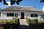 Diagonally opposite the Drostdy and immediately next to the Old Gaol, there is a small house with a thatched roof and thick walls. High up in the heavy yellow-wood front door there is a slot for receiving letters. This little building, still known as the Old Post Office was the residence of the gaoler. In the earliest days of the postal service at the Cape, the salary of a postmaster was so small that the appointment was held by someone who also performed some other Type of site: Post Office Previous use: Post office.