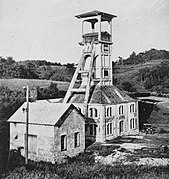 Photo noir et blanc d'un bâtiment carré surmonté d'une tour en béton équipée de deux bigues de contrefort.