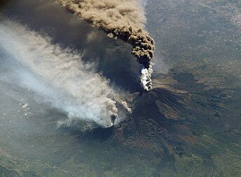 Éruption de l'Etna du 30 octobre 2002, photographiée depuis la station spatiale internationale. On peut voir le panache éruptif émis par le cratère sommital, ainsi que des incendies causés par des coulées de lave en contrebas. Les poussières du panache sont charriées vers le sud-est par les vents de basse altitude puis plein sud à plus haute altitude. Des cendres sont ainsi tombées sur la Libye, à plus de 500 km de distance. L'éruption de 2002 est l'une des plus vigoureuses éruptions de l'Etna ces dernières années. Aucun village n'a cependant été détruit par les coulées de lave. (définition réelle 2 720 × 2 000)