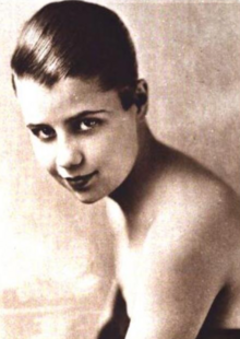 A young white woman with slicked-back short dark hair, wearing a strapless top
