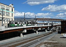 A light rail train on a curved bridge passing over a rail line in an urban area