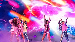 Maléna performing with four dancers and a colourful background behind her