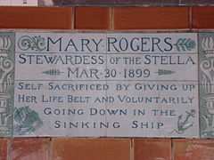 A tablet formed of two large tiles, bordered by green flowers in the style of the Arts and Crafts movement, and decorated with a stylised ship and anchor. The tablet reads "Mary Rogers, Stewardess of the Stella, March 30, 1899, Self sacrificed by giving up her life belt and voluntarily going down in the sinking ship".