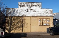 Photograph of the Vinsonhaler Blacksmith Shop, a one-story, brick, commercial/industrial building on a city streetside, with a wooden false front hiding the roof