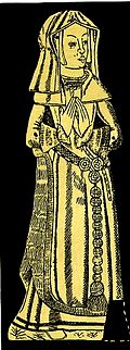 A woman in a long gown standing with hands clasped prayer-like in front of her. She wears a gable hood.