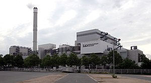 Das Müllheizkraftwerk Darmstadt vor einem bewölkten Himmel, davor eine Reihe Bäume.