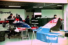 Photo d'un garage de course, dans lequel se trouve une monoplace bleue et blanche démontée