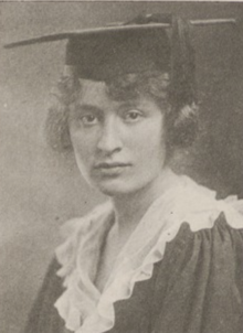 A young white woman wearing a mortarboard cap and academic robe with a white ruffled collar