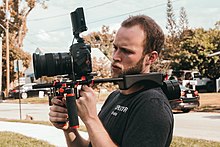 A videographer using a DSLR camera mounted on a shoulder rig. Videographer-using-DSLR.jpg