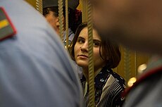 Женщина с каштановыми волосами и рубашкой с цветочным рисунком. Виду Самуцевич мешают два офицера в форме, стоящие перед ней.