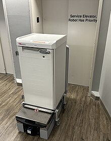 A hospital delivery robot in front of elevator doors stating "Robot Has Priority", a situation that may be regarded as reverse discrimination in relation to humans Hospital delivery robot having priority to elevators.jpg