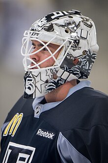 Photographie d’un gardien de hockey sur glace, vu depuis la hauteur du torse de trois-quarts face, le masque devant le visage.