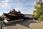 A large wooden building with two small gabled roofs put on top of the main roof and across the main ridge. There are forked roof finials on the top.