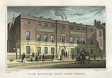 This image shows the London Lock Hospital from the street in the late 18th century. It is a red brick building in the Georgian style on a busy street.