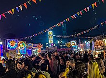 People gather around food booths lit up by neon signs in vibrant colors.