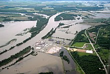Aerial view of farms and a power station in a rural area partly inundated by a river that has overflowed its banks