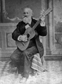 Photographie en noir et blanc représentant Iparraguirre jouant de la guitare assis sur un tabouret