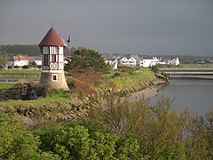 Photographie montrant la rive d'un cours d'eau visible à droite, surmontée d'un petit moulin sur la droite.