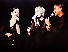 Image of a three females. They are wearing black and holding michophones.