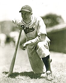 A baseball player is kneeling with one knee while leaning onto a baseball bat.