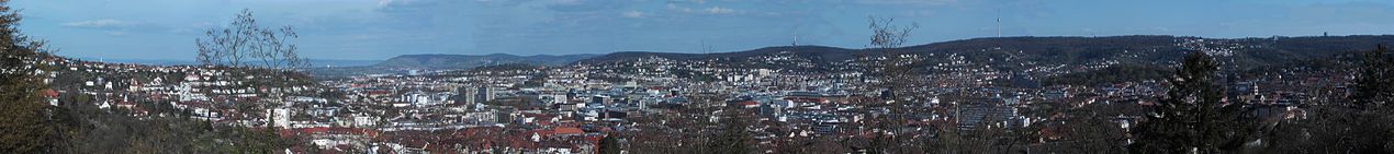 Panorama Stuttgartu z południowego wschodu. Od doliny Neckar z lewej miasto wznosi się w kierunku centrum, przesłaniane przez wysokie drzewa w stronę wieży telewizyjnej na południu. Po prawej Stuttgart południowy i zachodni.